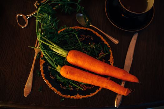 A close-up of three vibrant carrots on a decorative plate with vintage silverware.