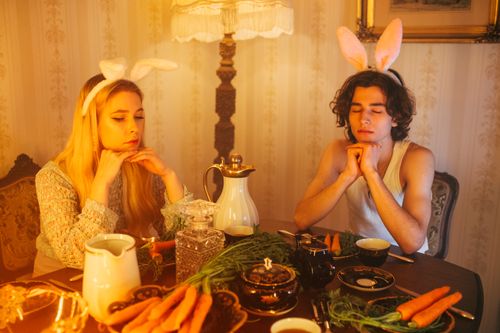 Free A whimsical dinner scene with two adults wearing bunny ear headbands, surrounded by carrots. Stock Photo