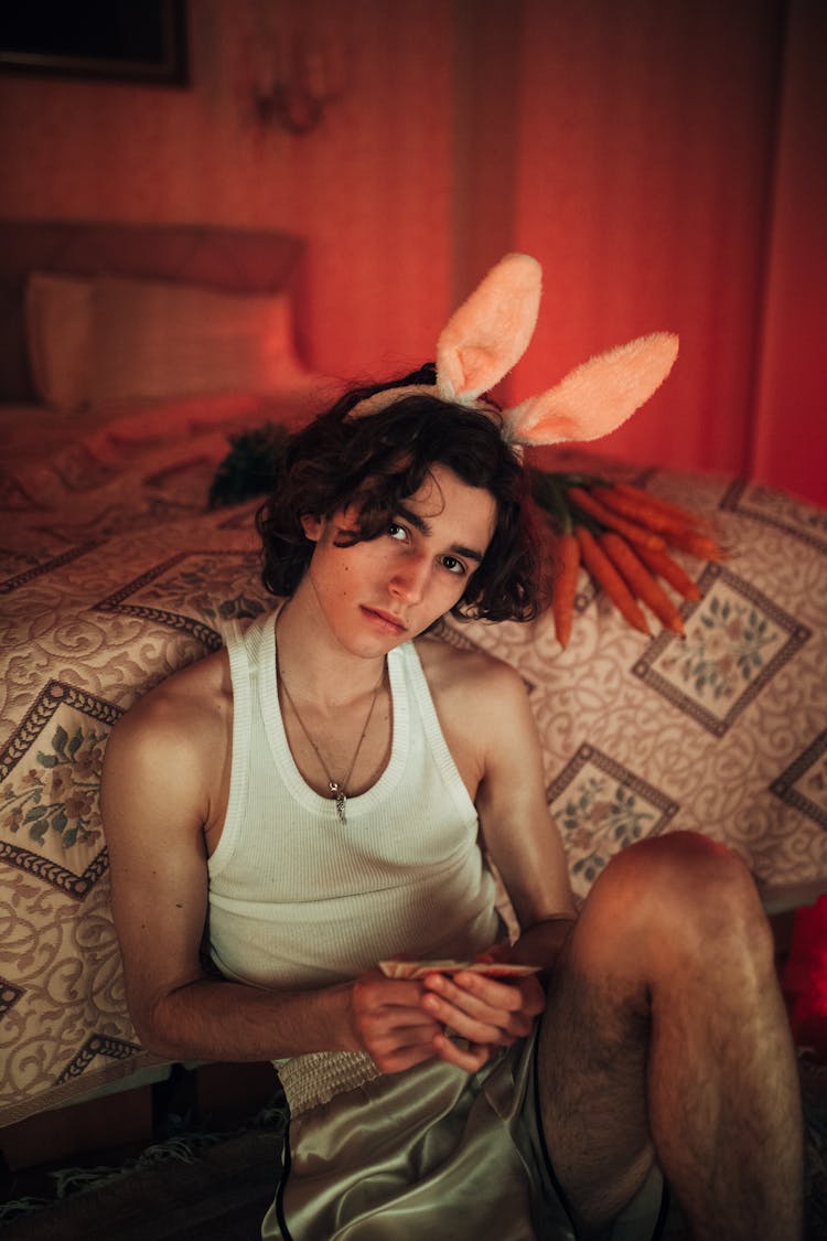 A Young Boy In White Tank Top Sitting Near The Bed