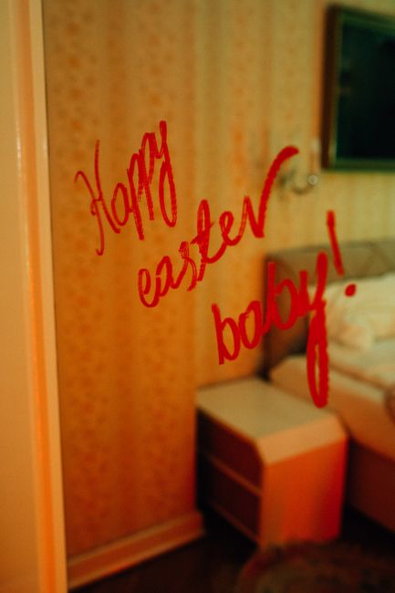 A mirror reflects a vibrant 'Happy Easter Baby!' message in vivid red color within a cozy indoor setting.