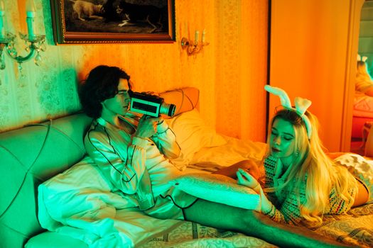 Stylish young couple in bed with retro camera and bunny ears, creating a vintage vibe.