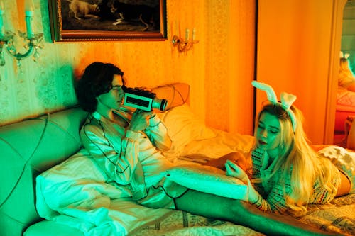 Stylish young couple in bed with retro camera and bunny ears, creating a vintage vibe.