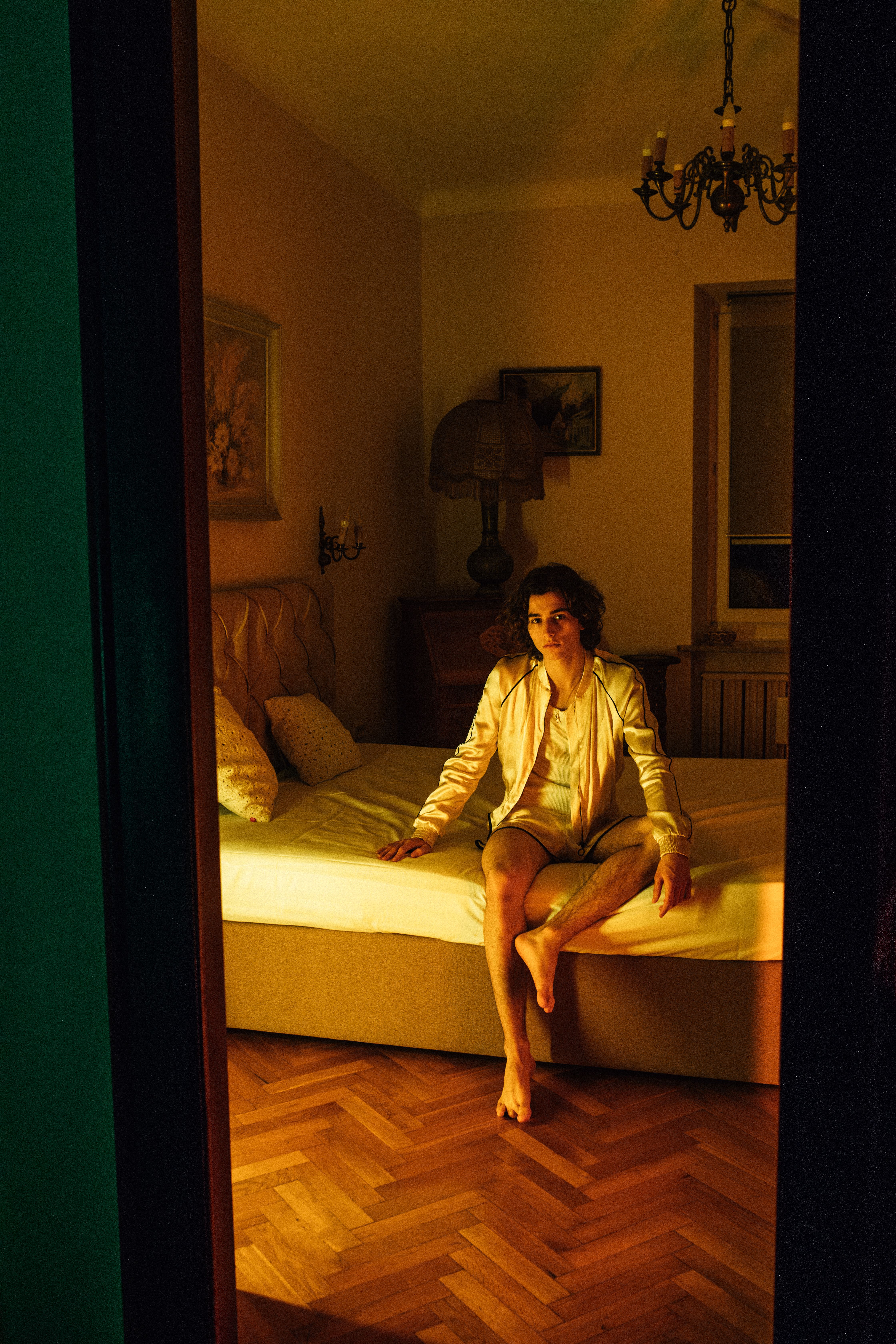 A man sits thoughtfully on a bed in a dimly lit room, creating a moody ambiance.
