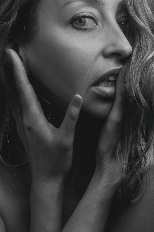 Free Close-up black and white portrait of a woman touching her face with an emotional gaze. Stock Photo