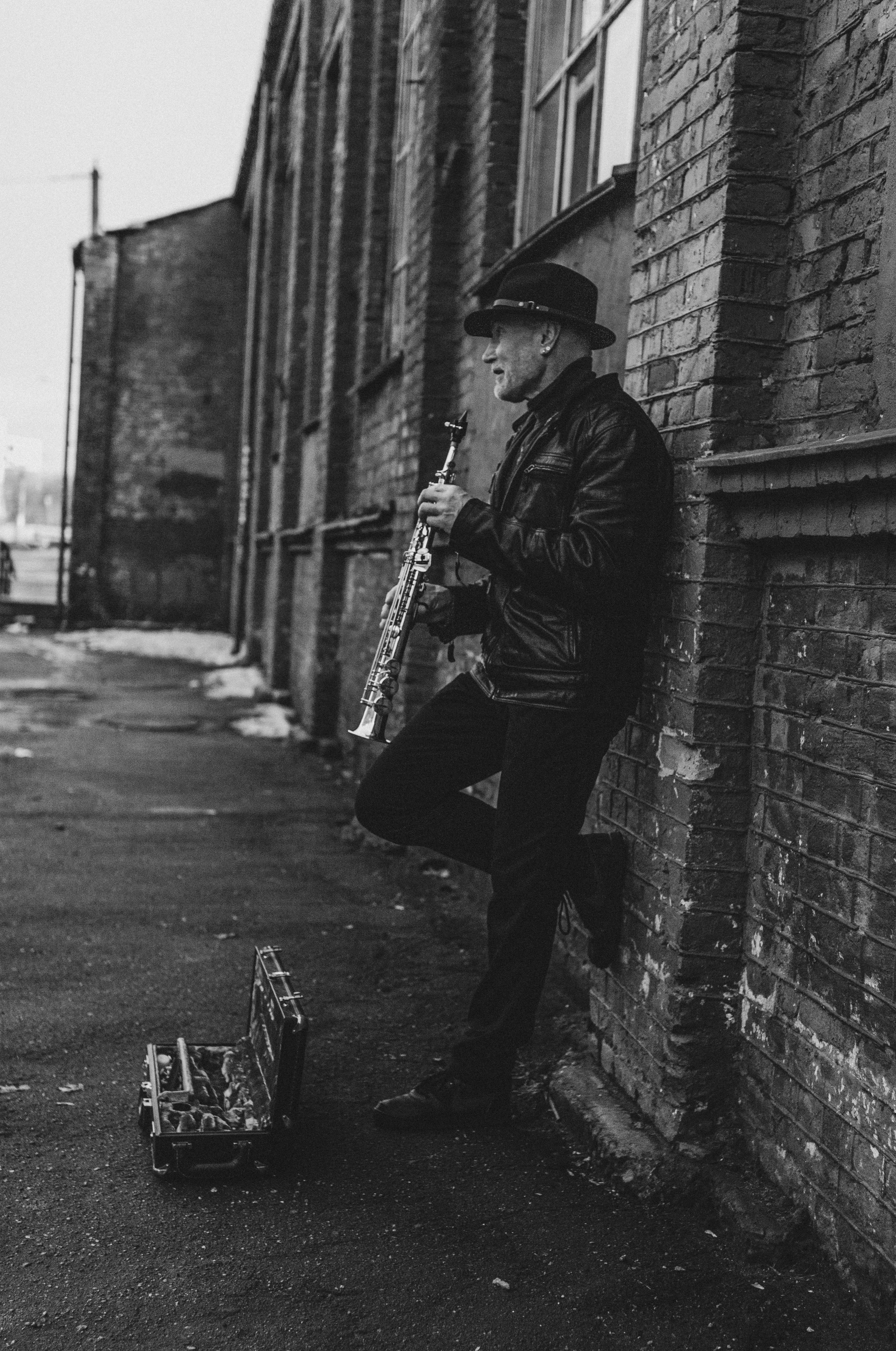 Black and white photo of a man in a leather jacket playing a clarinet outdoors.