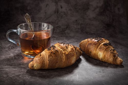 Free Fresh croissants paired with a cup of hot tea on a rustic table setting. Stock Photo