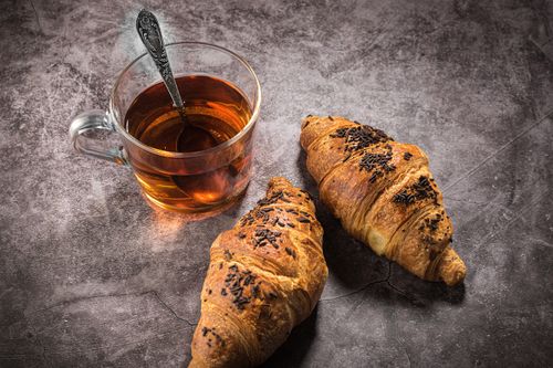 Free Two freshly baked croissants with a cup of hot tea on a rustic stone surface. Perfect for breakfast. Stock Photo