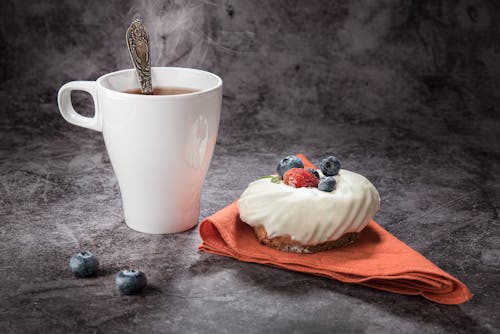 A Cup of Hot Tea Beside a Bread Topped with Berries