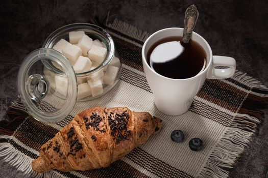Elegant breakfast setting with a croissant, coffee, and sugar cubes on a textured cloth.