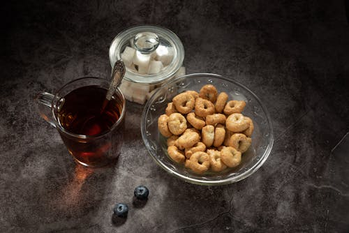 Free Glass of Tea Beside a Bowl of Cereals and a Glass Jar of Sugar Cubes Stock Photo