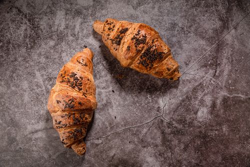Free Two freshly baked chocolate chip croissants on an earthy textured surface, perfect for food photography. Stock Photo