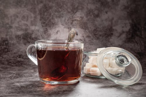 Clear Glass Cup With Tea Beside a Jar of Sugar Cubes