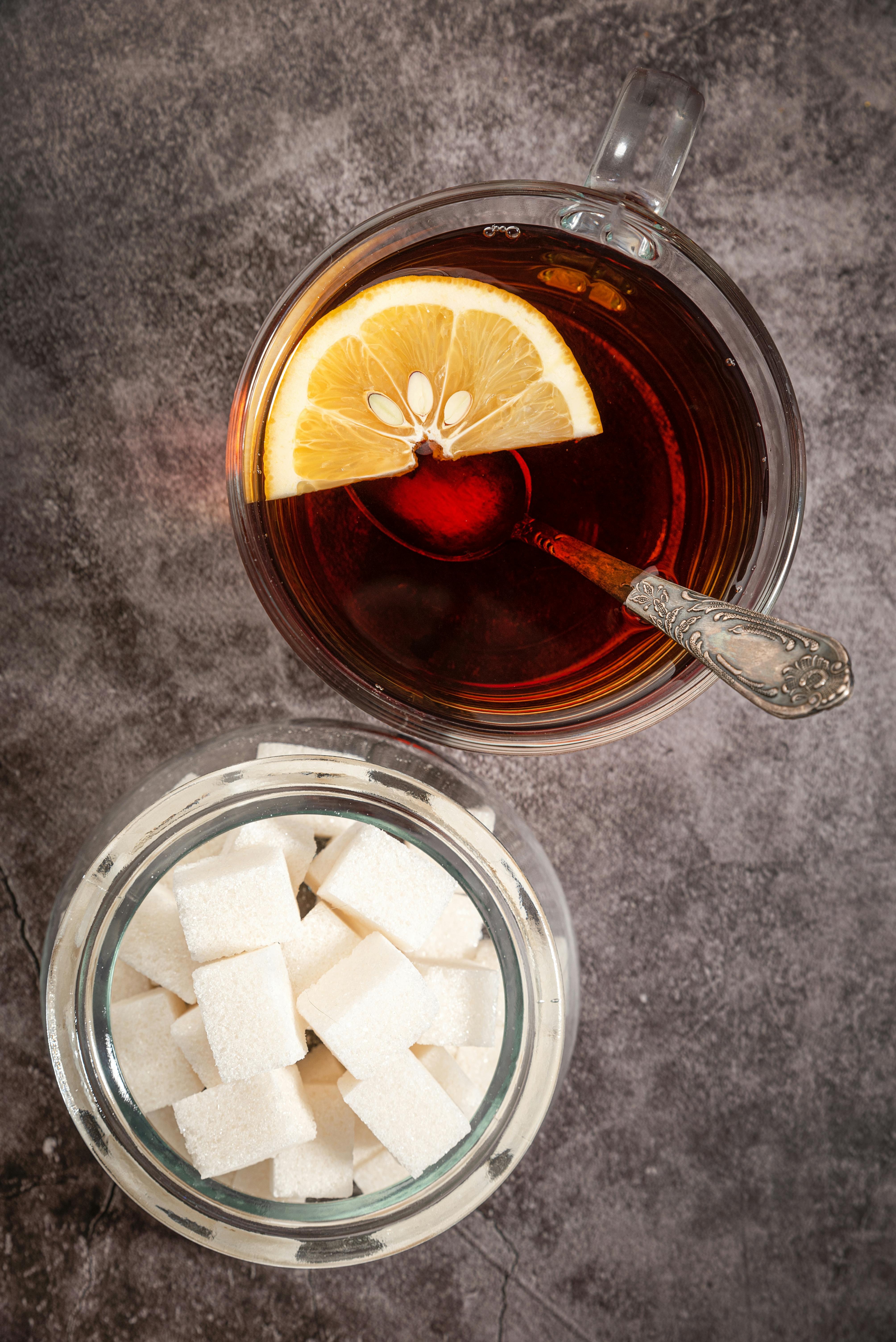 slice of lemon and teaspoon on glass of tea beside a jar of sugar cubes