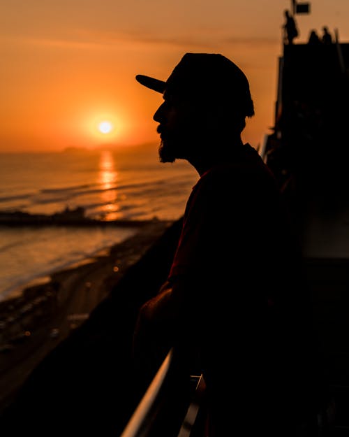 Free A Man Standing Beside a Railing Looking Afar during Sunset Stock Photo