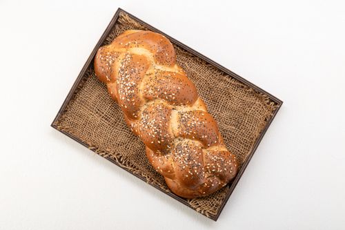 Free Overhead shot of a golden braided challah bread with sesame seeds, presented on a rustic woven tray. Stock Photo