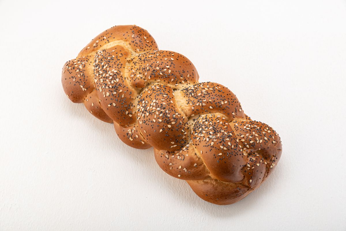 Braided challah loaf with sesame and poppy seeds on a light surface