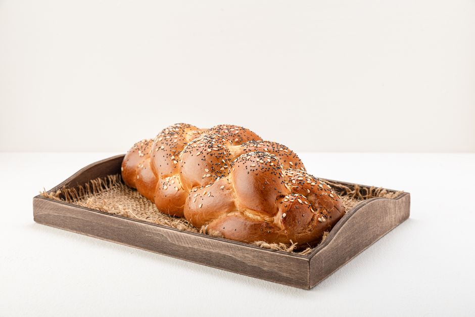 Delicious homemade challah bread with sesame seeds and poppy seeds, placed on a rustic wooden tray.