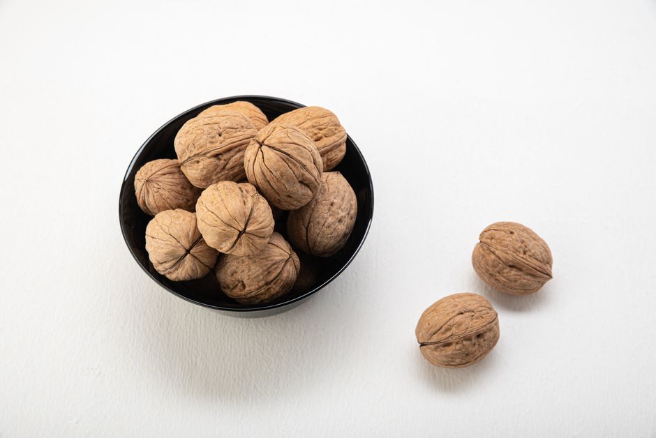 Top view of fresh walnuts in a black bowl on a white background, emphasizing healthy snacking. - Types of Healthy Snacks Available in Pakistan