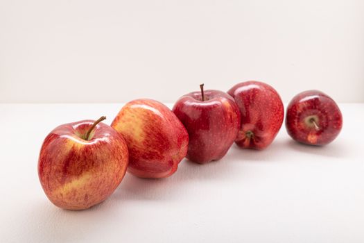 Five fresh red apples perfectly arranged on a clean white surface, highlighting their vibrant color and texture.