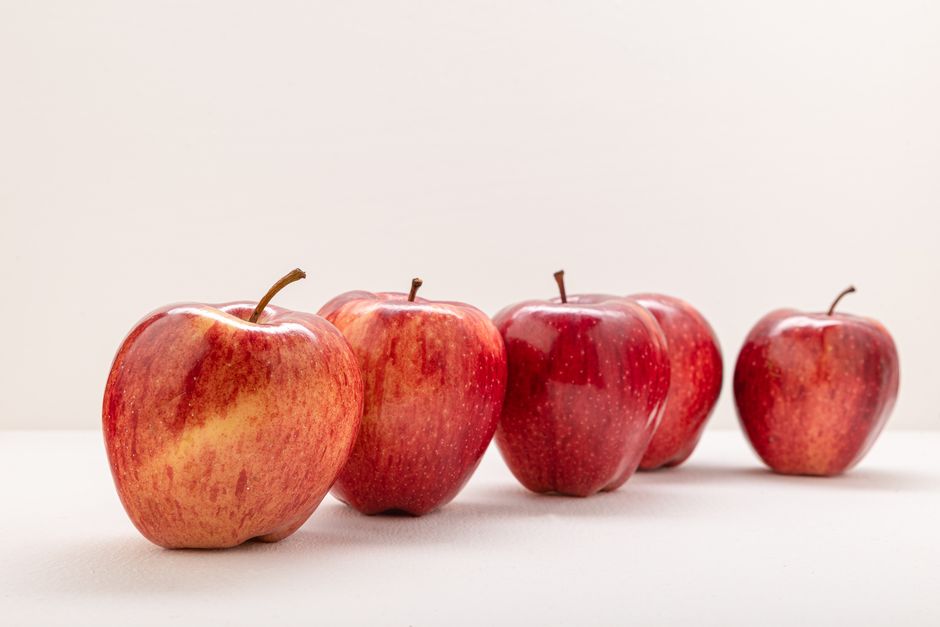 Five fresh red apples lined up on a white surface, showcasing healthy eating.