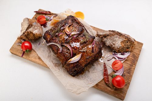 Free Savory grilled meat garnished with onions, tomatoes, and rustic bread on a cutting board. Stock Photo