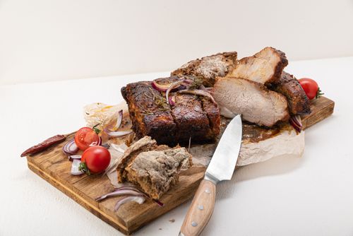 Free Juicy roast pork slices on a wooden board with tomatoes and red onions, ready to serve. Stock Photo
