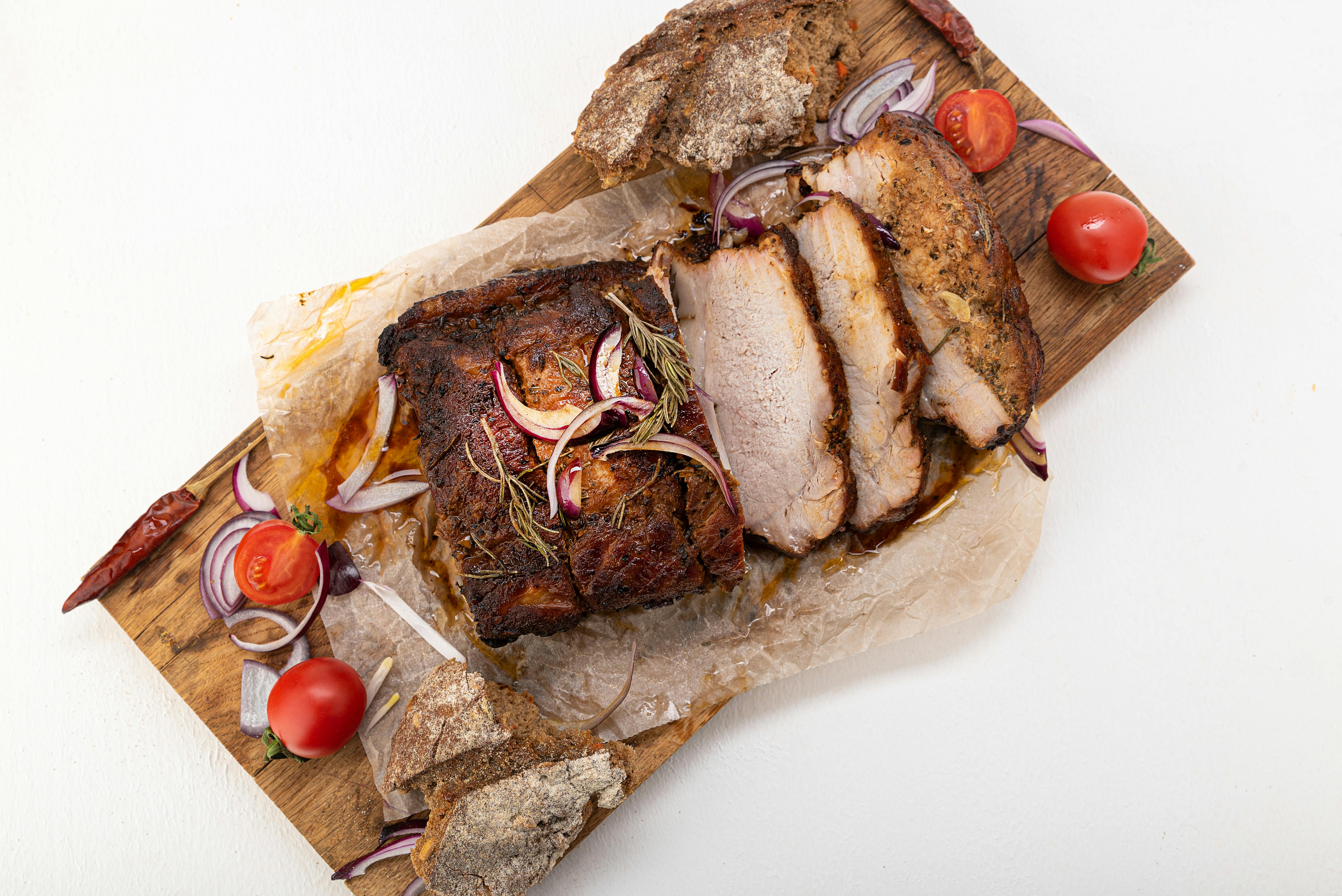 Sliced roasted meat with tomatoes and onions on a wooden board. Perfect for BBQ lovers.