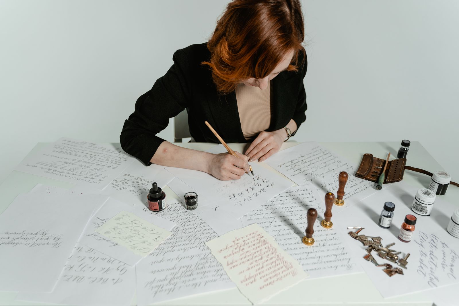 Letterer inking a brush-lettered sheet at a white studio desk — photo by MART PRODUCTION on Pexels