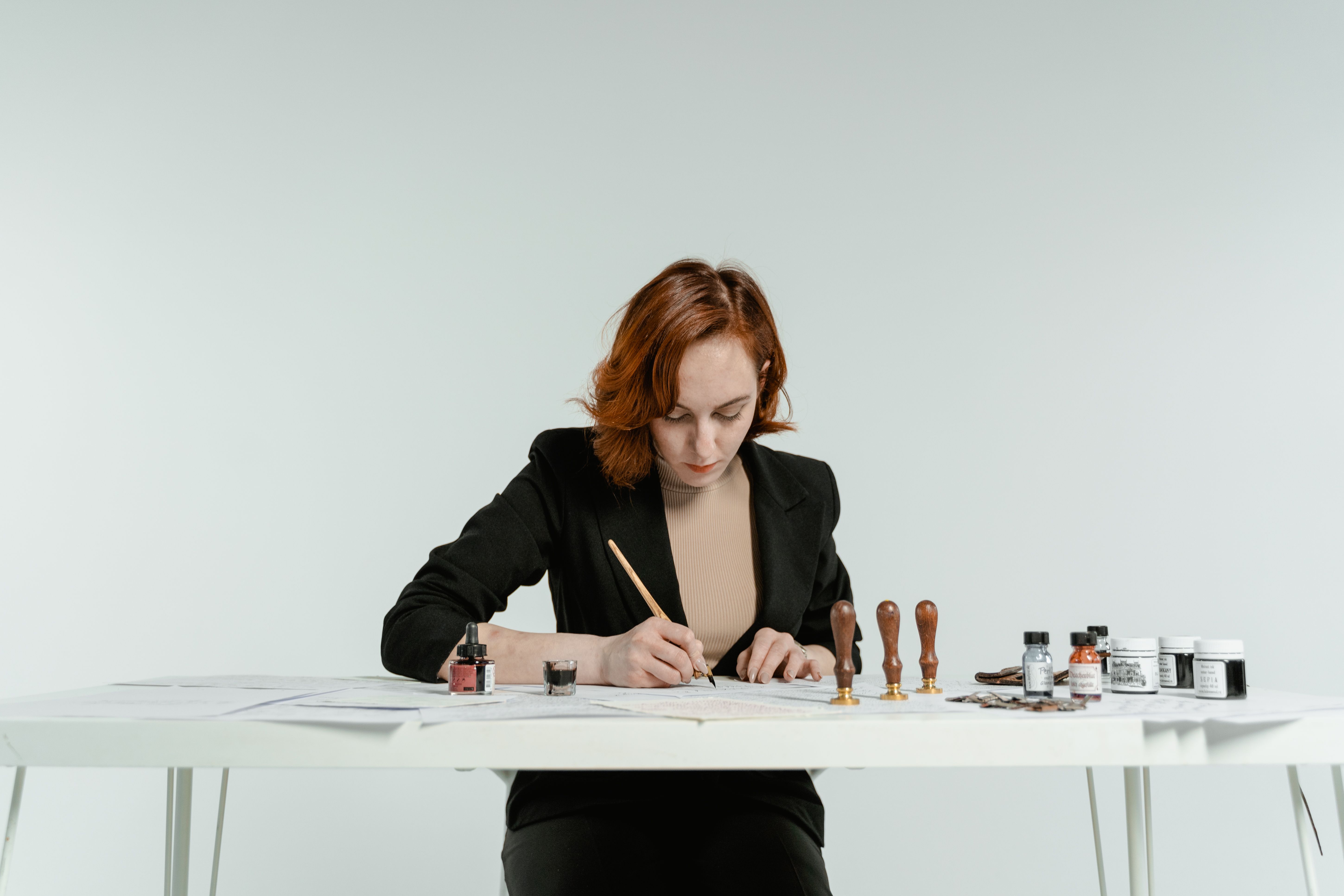 Caucasian woman focused on calligraphy practice with tools on a white table.
