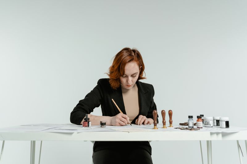 Caucasian woman focused on calligraphy practice with tools on a white table.