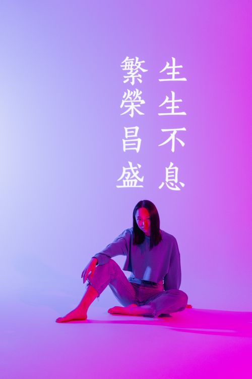 Free Asian woman in purple lighting sitting in denim, illuminated by projector with Chinese text. Stock Photo