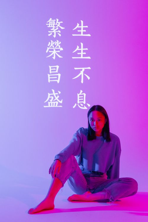Free Asian woman seated in a studio with neon Chinese calligraphy, creating a vibrant and modern look. Stock Photo