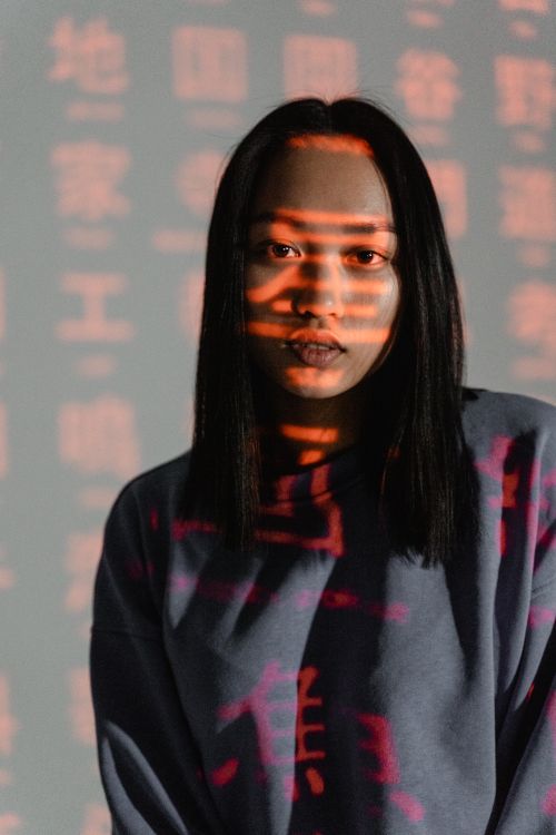 Free Portrait of an Asian woman with red text projected on her face, creating a dramatic effect. Stock Photo