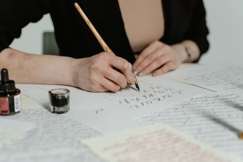 Free Close-up of a person's hands practicing calligraphy with ink and pen. Stock Photo