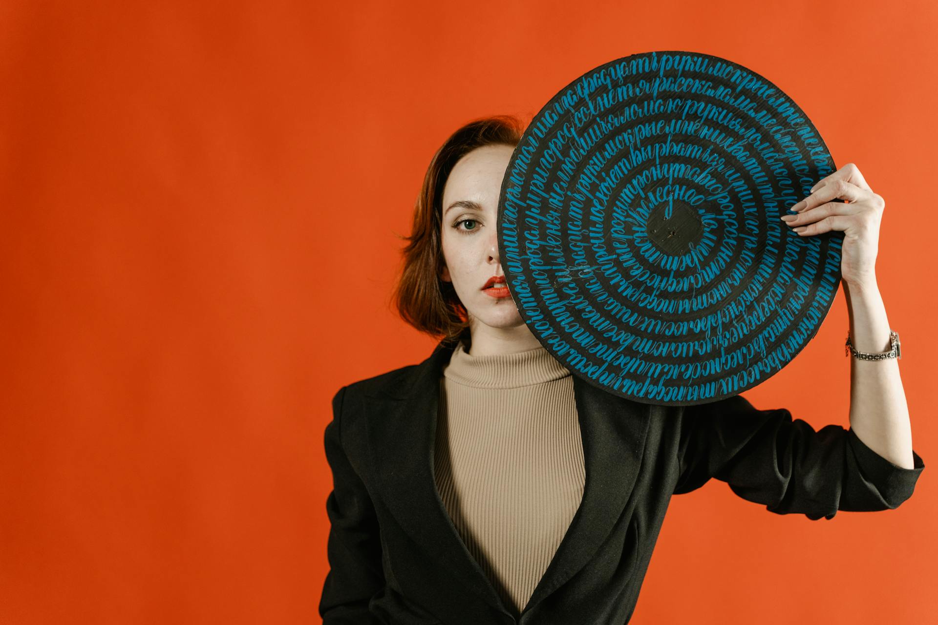 Woman in Black Blazer Holding a Round Board with Handwriting Covering Her Eye