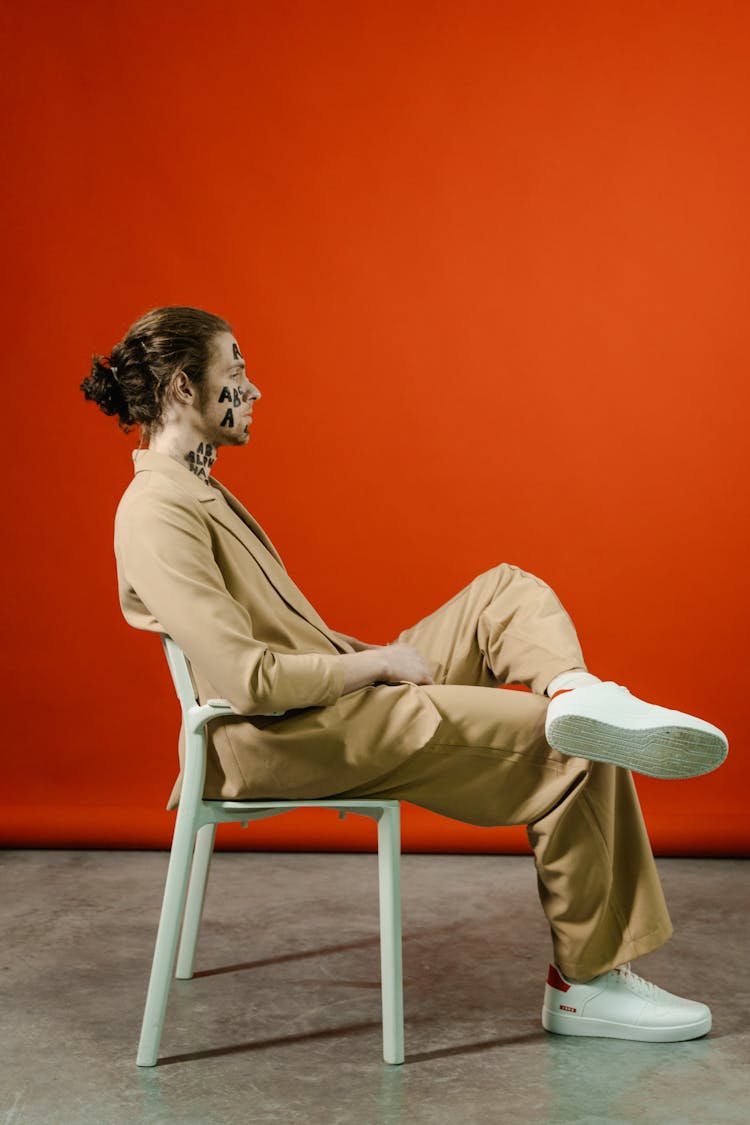 

A Man In A Beige Suit Sitting On A Chair