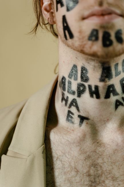 Artistic close-up of letters on a person's neck with facial hair and neutral background.