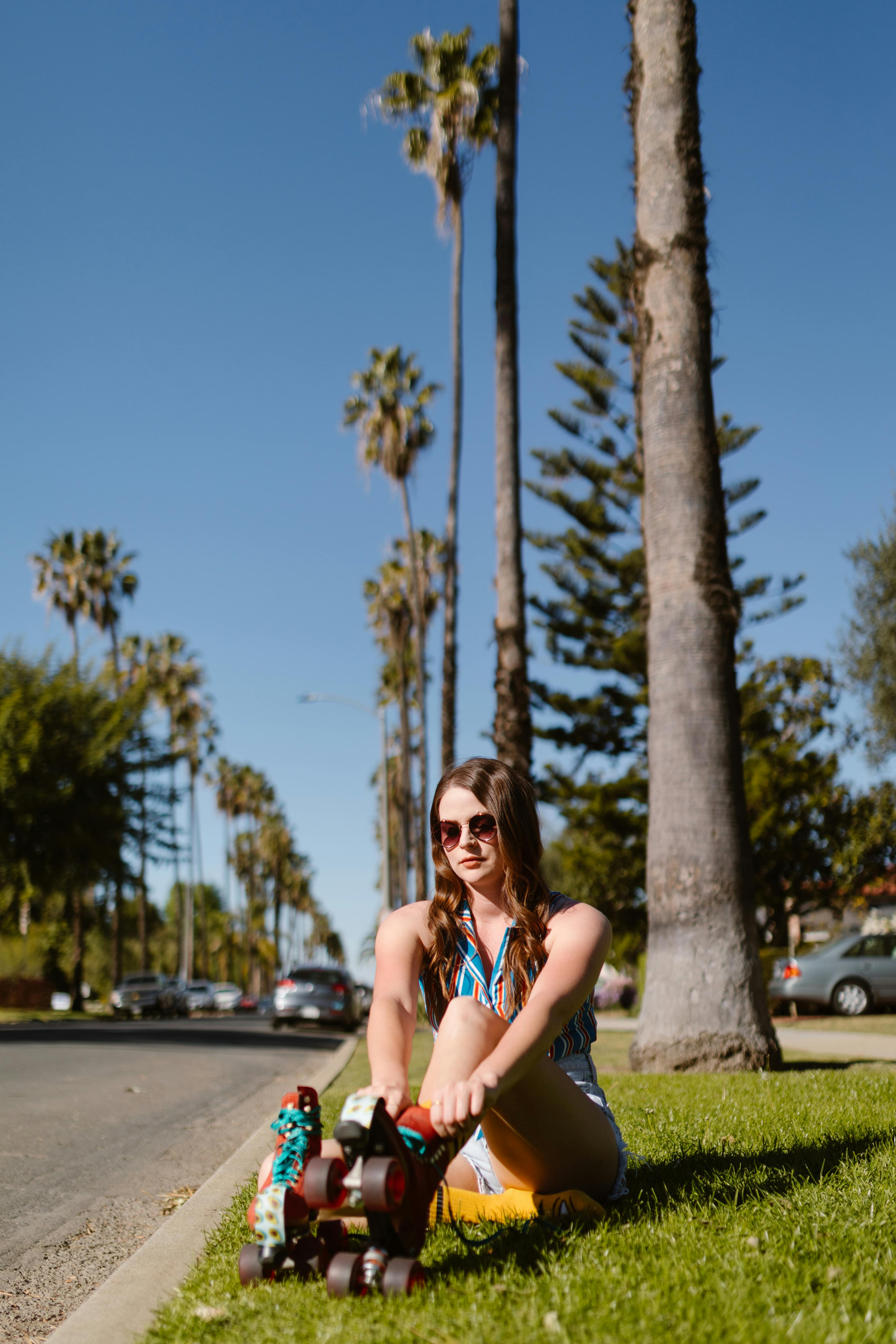 Young woman in roller skates sitting on grass, enjoying a sunny day under palm trees.