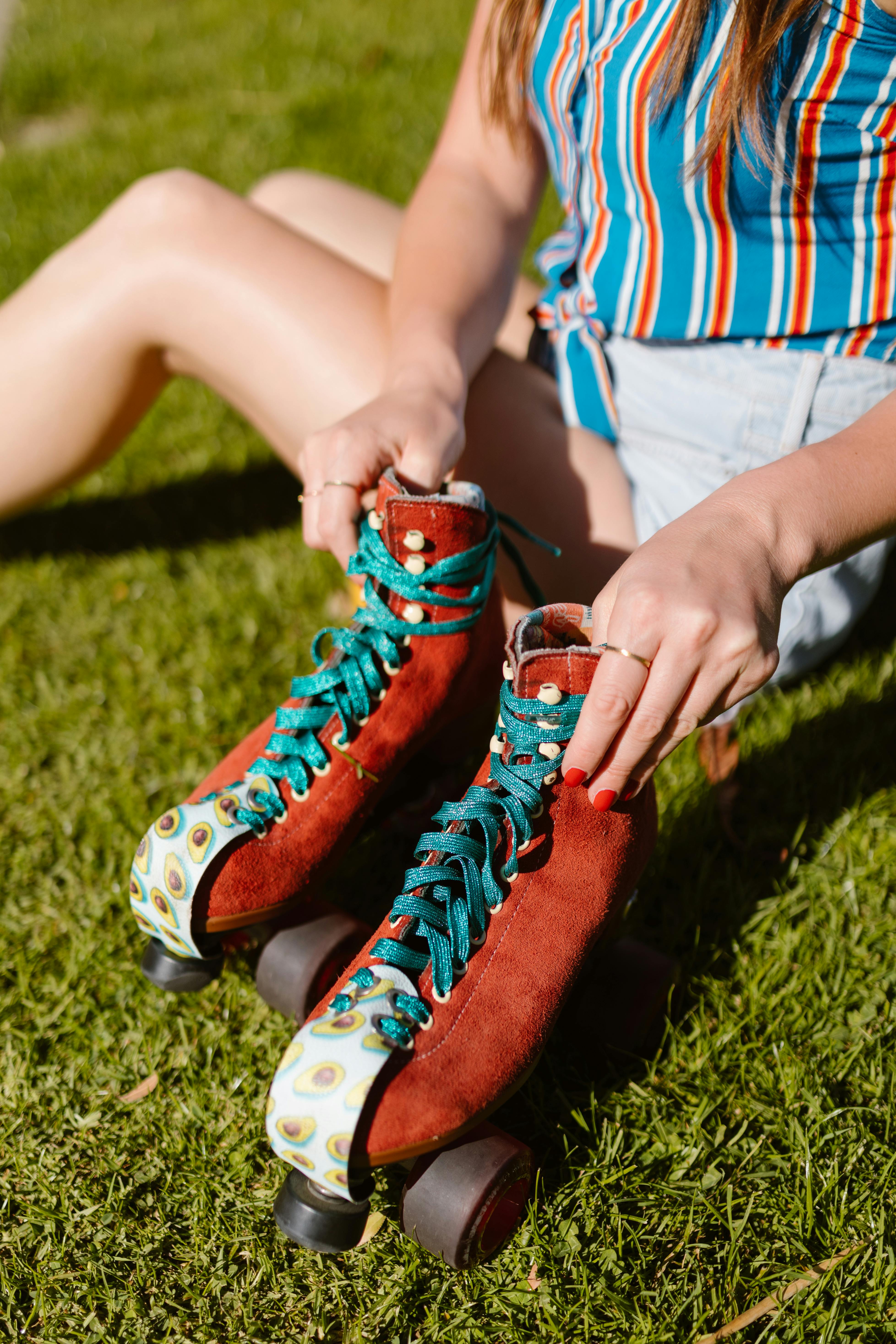 A young woman sits on grass adjusting her red roller skates on a sunny day.