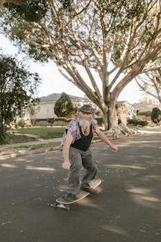 Elderly man enjoys skateboarding outdoors on a sunny street surrounded by large trees.