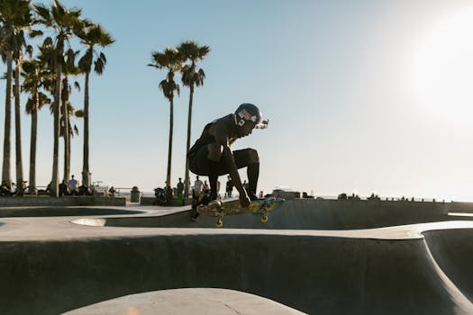 A skateboarder performs an aerial trick in the vibrant Venice Beach skatepark under a sunny sky.