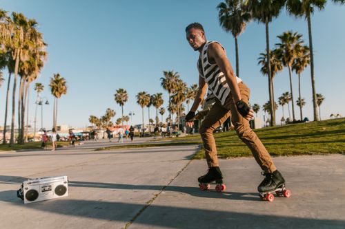Free A man roller skating on a sunny day with palm trees and a cassette player nearby. Stock Photo