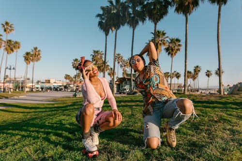 Women Wearing Sunglasses and Roller Skates Sitting on Grass Field 