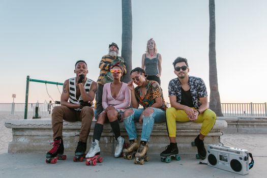 A vibrant group of adults in roller skates sitting together at the beach with a boombox, enjoying a sunny day.