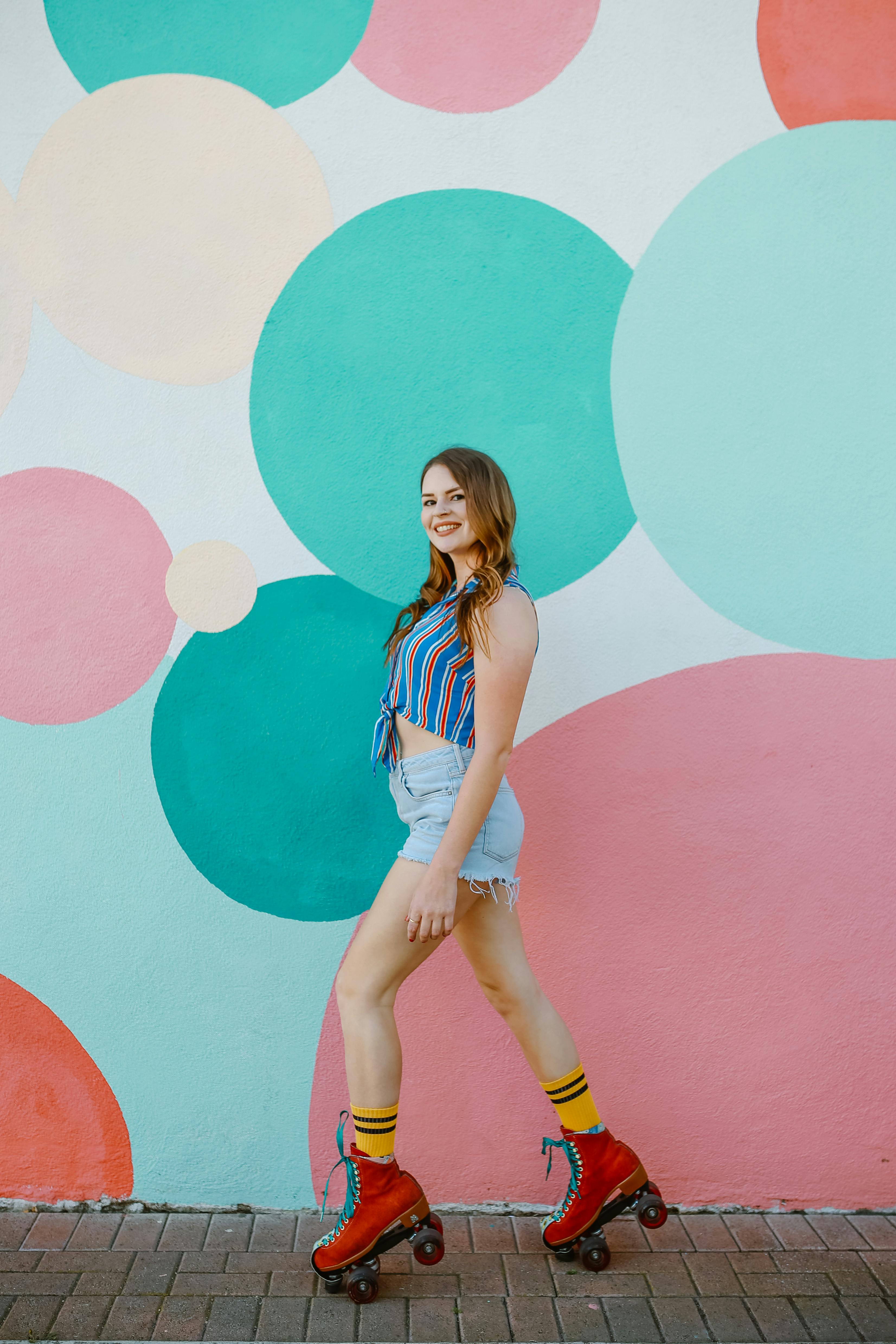 woman in blue and white stripe shirt and white shorts standing beside pink wall