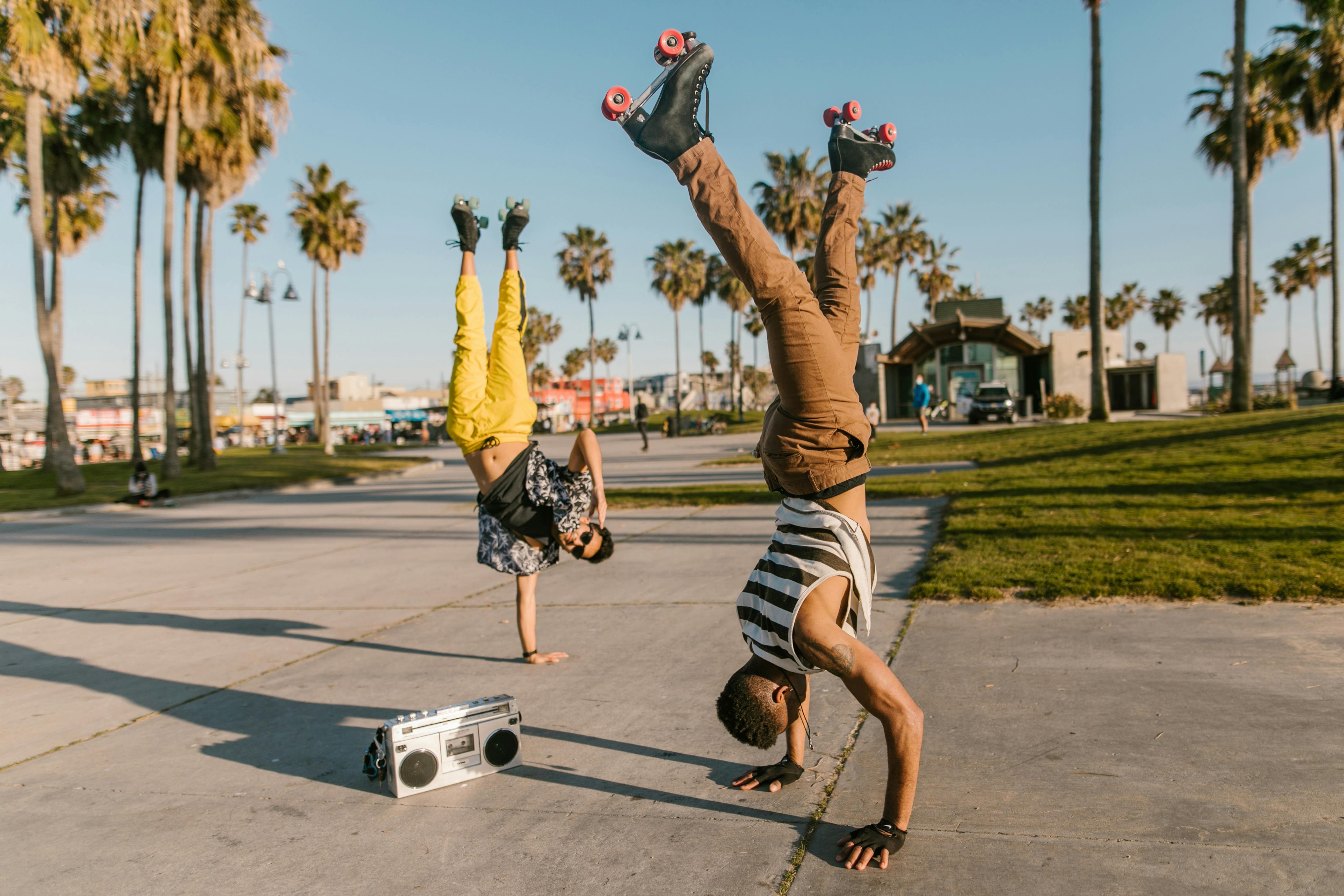 Two young men performing handstands on Venice Beach with a boombox nearby, showcasing fun and fitness.