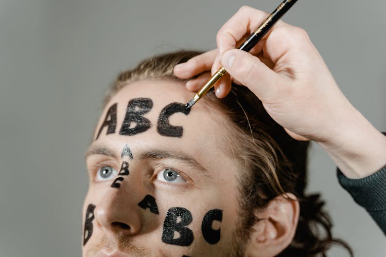 A Person Writing Letters On A Man's Face