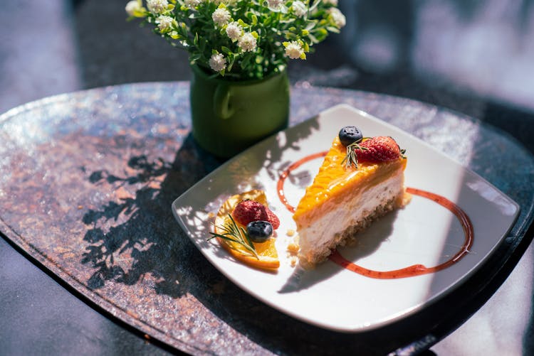 Delicious Piece Of Fruit Cake And Small Vase Of Flowers