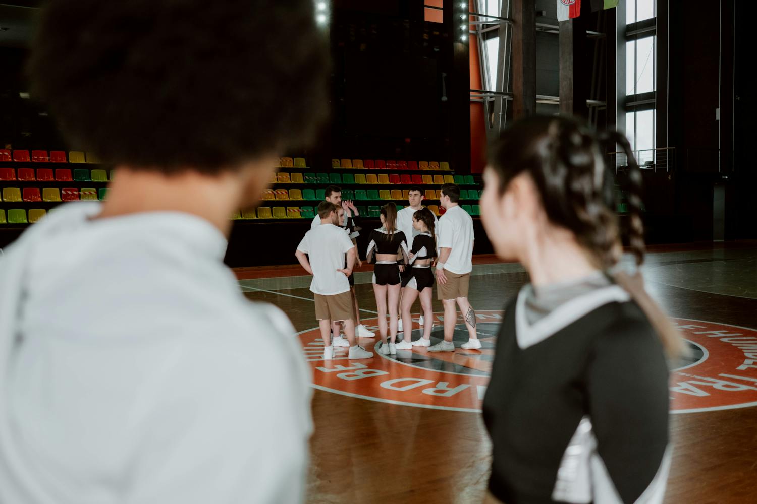 A cheerleading team gathers for practice in a brightly lit gymnasium.