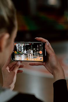 A person recording a cheerleading group with a smartphone during practice indoors.
